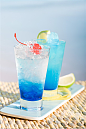 阳光海边竹垫上的蓝色冰镇水果柠檬鸡尾酒果汁