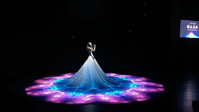 歌手身穿洁白巨型拖地长裙在巨大的舞台运用全息投影技术结合现场光影